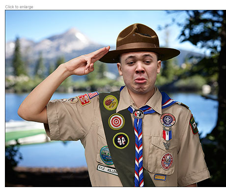 A saluting Kyle Rittenhouse as a Scout in the Bullshit Artists with merit badges for Rifle Shooting and Theater.