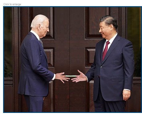 Satirical photo-illustration of President Joe Biden of the United States meeting with Premier Xi Jinping of the People's Republic of China by reaching out his hand for a handshake, but his and Xi's index fingers are stuck in a gag toy Chinese fInger trap.